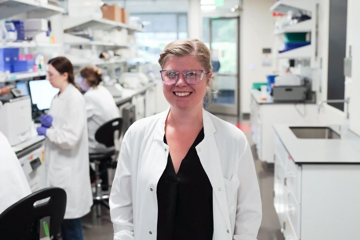 Image of immunologist Claire Gustafson. She wears glasses and smiles at the camera while wearing a black shirt under a white lab coat. Image of immunologist Claire Gustafson. She wears glasses and smiles at the camera while wearing a black shirt under a white lab coat.