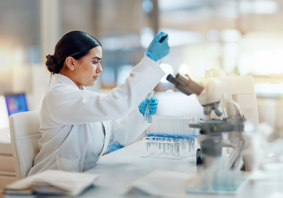 An individual working at a scientific bench in front of a microscope. An individual working at a scientific bench in front of a microscope.