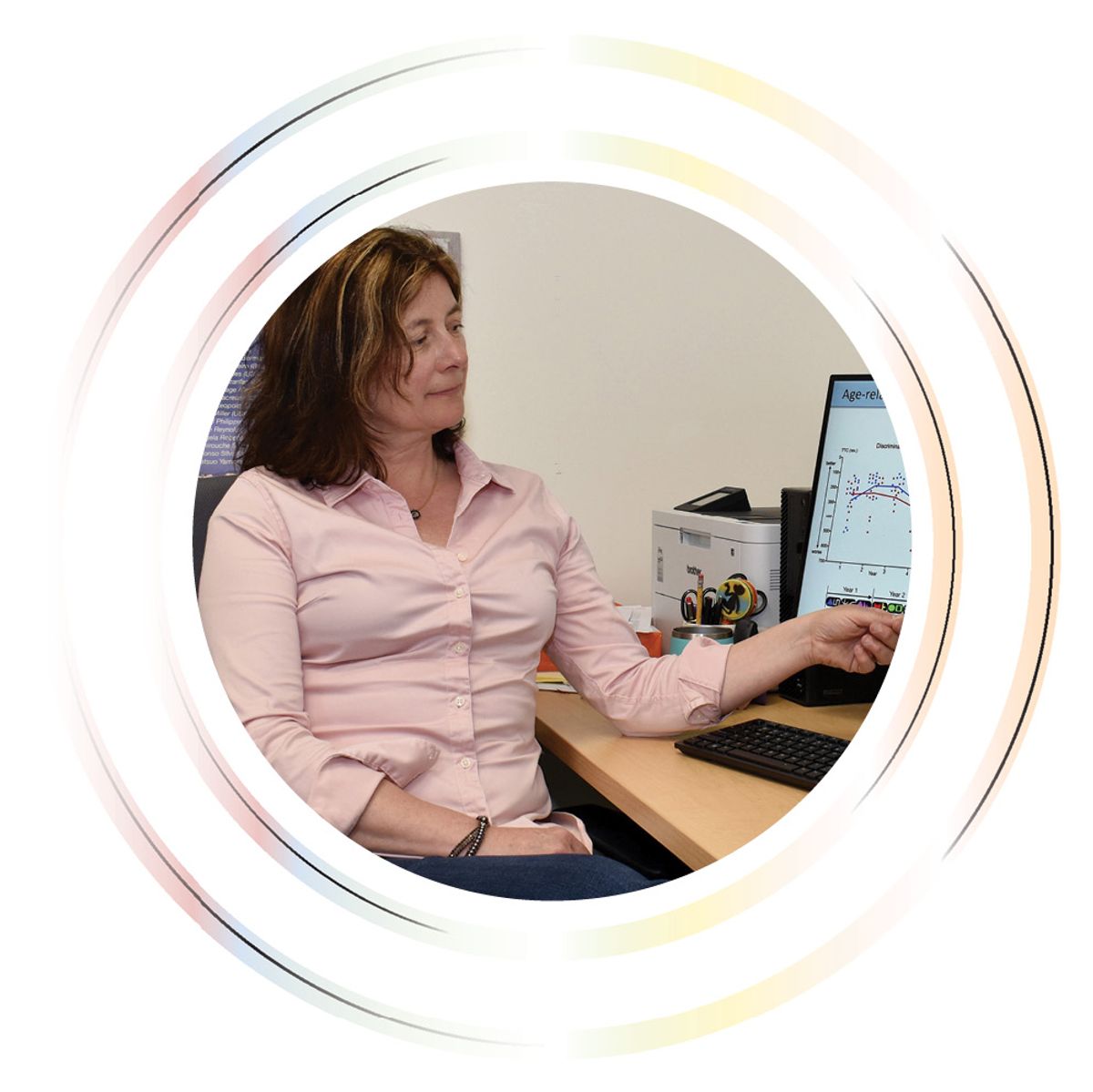 A woman sits at her desk while gesturing to an image on the computer screen next to her. A woman sits at her desk while gesturing to an image on the computer screen next to her.