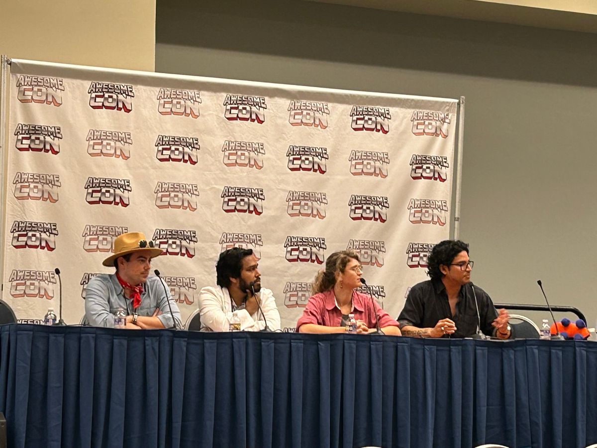 Carlo Quintanilla (far right) speaks at a panel table for a science-fiction conference, joined with three other panelists. He has dark hair and is wearing a dark gray shirt. Carlo Quintanilla (far right) speaks at a panel table for a science-fiction conference, joined with three other panelists. He has dark hair and is wearing a dark gray shirt.