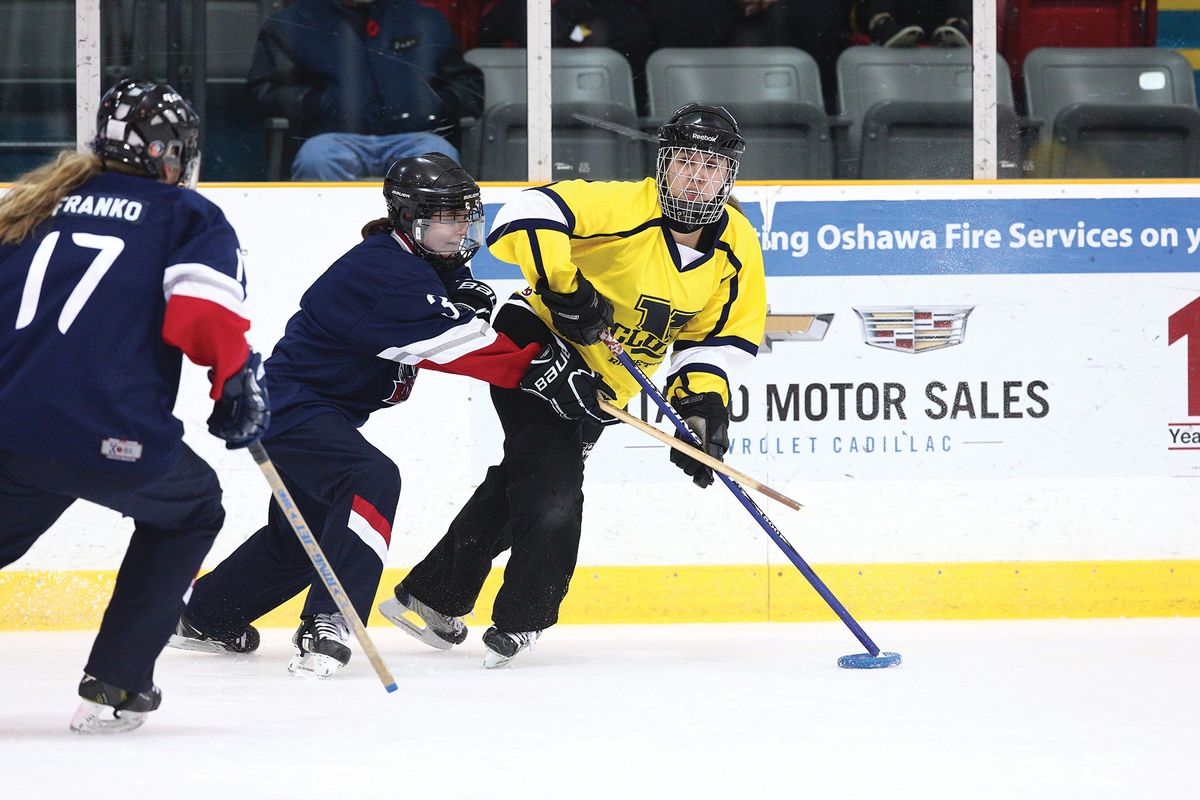 Image of three ringette players on an ice rink. Two players are in blue, red, and white jerseys. Melissa Kay is pictured in the yellow jersey. Image of three ringette players on an ice rink. Two players are in blue, red, and white jerseys. Melissa Kay is pictured in the yellow jersey.