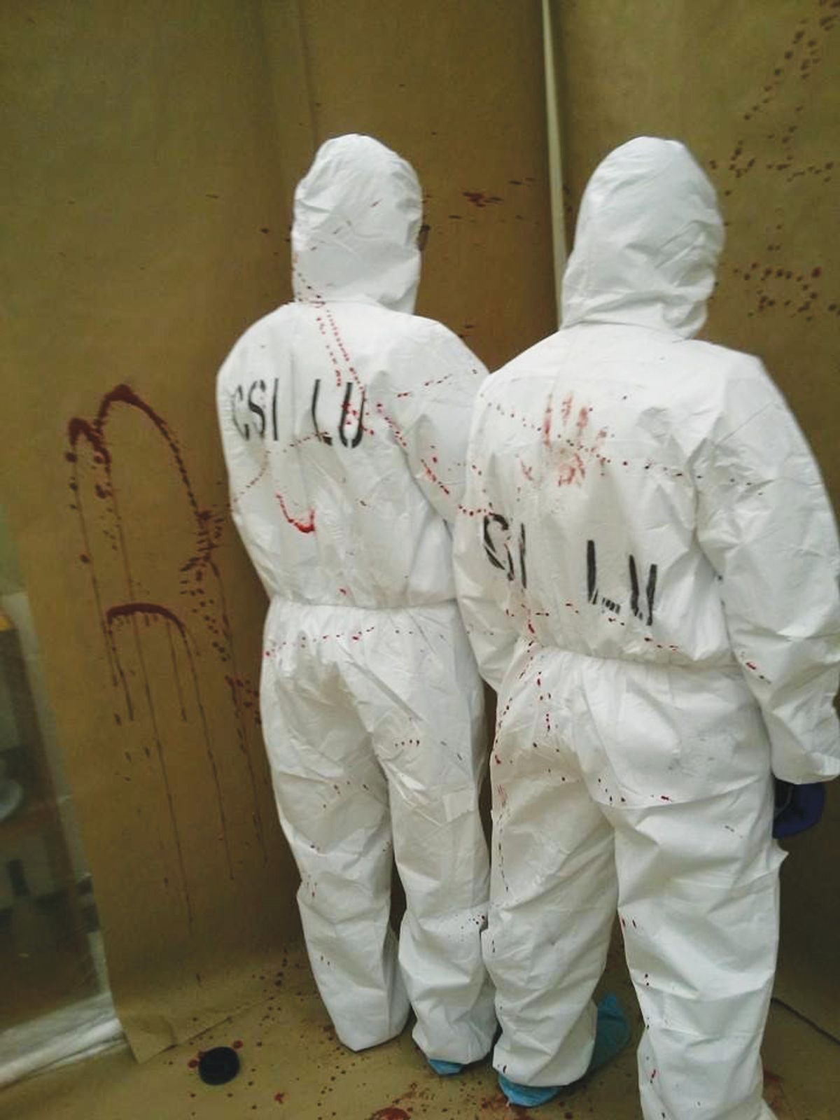 Image of Melissa and a classmate wearing white bunny suits in a blood spatter lab. Image of Melissa and a classmate wearing white bunny suits in a blood spatter lab.